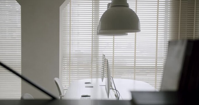 Quiet and empty modern office interior with a clean desk, computer, and chair near a window with closed blinds, creating a calm and professional atmosphere for corporate work or study