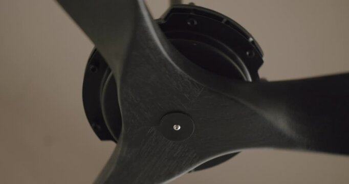 Slow motion, low angle shot of a modern black ceiling fan with three blades turning and cooling the air in a room. Interior design detail showing a contemporary ventilation system