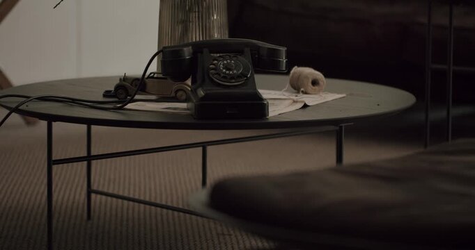 Slow motion view of a classic black rotary telephone resting on a modern dark table in a cozy living room, symbolizing nostalgia, communication history, and timeless interior design details
