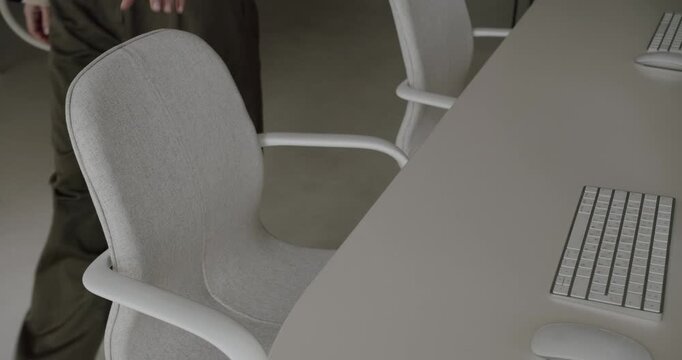 High-angle slow-motion footage of a person's hands pulling out a modern ergonomic chair from a minimalist white desk in a contemporary, clean office space, ready to start working