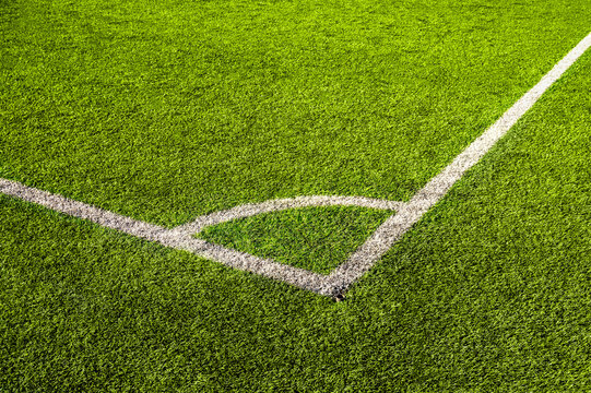 Top view of green artificial grass with white marking lines on soccer field. Football pitch corner kick area with synthetic turf. Athletic sports ground texture background