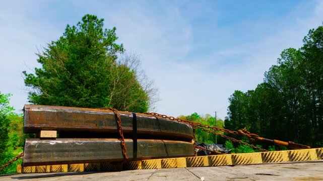Industrial steel beams secured with binding chains and straps on a flatbed trailer, illustrating heavy cargo transport, raw material supply chains, and B2B freight distribution.