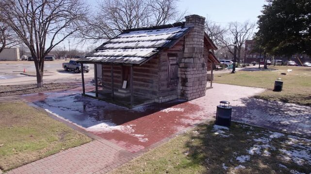 4K drone pullback footage of the historic Larkin Newton Log Cabin in downtown Midlothian, Texas, showcasing local heritage, pioneer architecture, and a significant historical landmark.