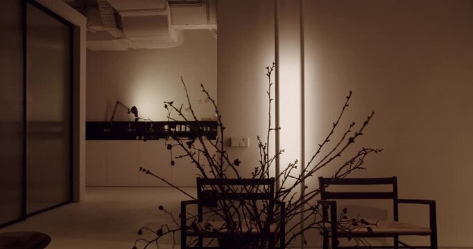 Serene and minimalist living room interior with a contemporary Japanese aesthetic, featuring a large ikebana-style branch arrangement, modern wooden chairs, and soft, warm ambient lighting
