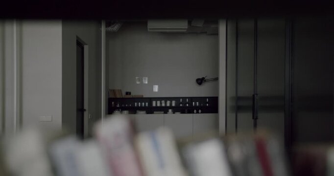 Slow-motion dolly shot revealing a modern office or clinic space through the gap in a bookshelf, with out-of-focus books creating a sense of depth and focus pulling towards the background