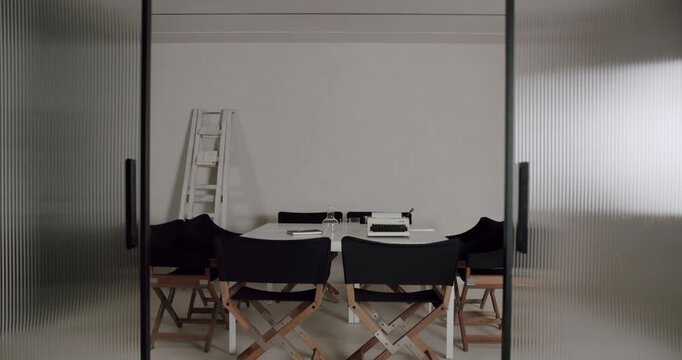 Modern translucent ribbed glass doors slowly sliding open to reveal a contemporary meeting room with a white table, director's chairs, and a vintage typewriter in an empty minimalist office
