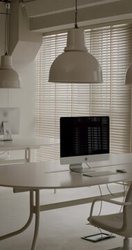 Modern and minimalist office interior featuring white desks with computers and comfortable chairs, bright and clean contemporary workspace for productive work and professional meetings. vertical