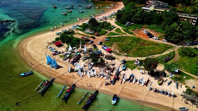 Fishing boats, small sailboats and beach activity fill the shallow turquoise shoreline of Weligama Bay in Sri Lanka.