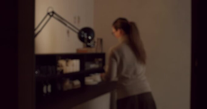 Out of focus shot of a woman with her hair in a ponytail getting dressed quickly in a dimly lit room after a romantic encounter, grabbing her clothes and rushing away from the scene