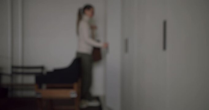 Blurry slow motion shot of a young woman with a ponytail entering a contemporary room with a white built-in wardrobe and a grand piano, the sunlight illuminating her from behind