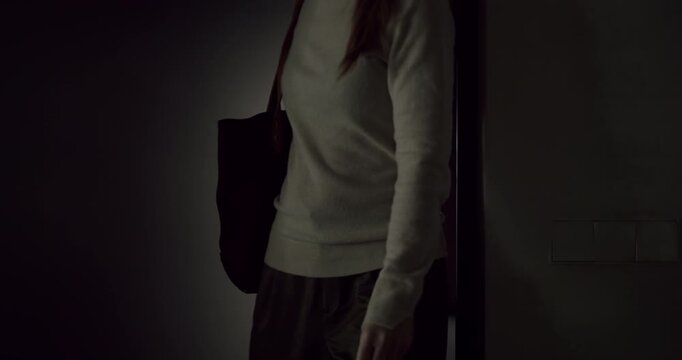 Woman with a bag opening the door and entering a dark room in slow motion, creating a mysterious silhouette against the light from the other side before the door closes behind her