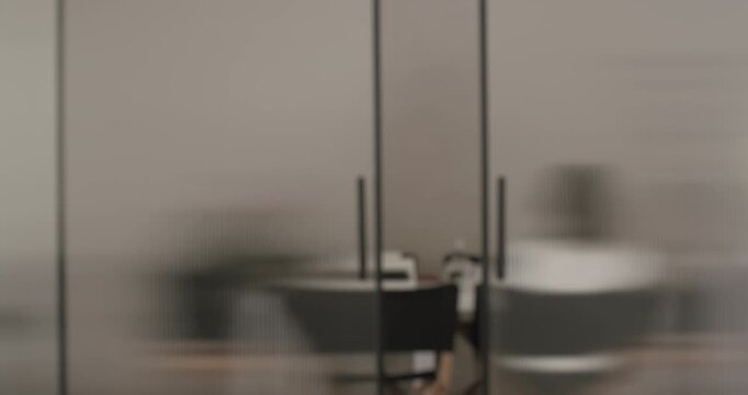 Blurred slow motion view of a young professional woman opening a sliding fluted glass door, walking into a modern office space and then the door closes automatically behind her