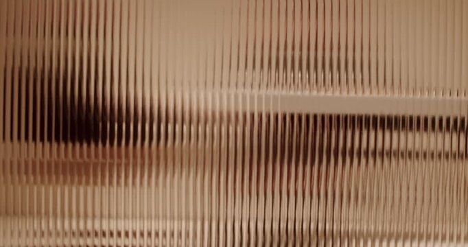 Blurred human silhouette walking behind a fluted glass wall creating a mysterious and distorted visual effect, with the unrecognizable figure casting a dark shadow as they move past