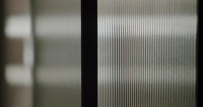 Slow motion close-up of a fluted glass surface moving, creating an elegant visual effect with distorted light reflections and a dynamic sense of motion for a sophisticated background
