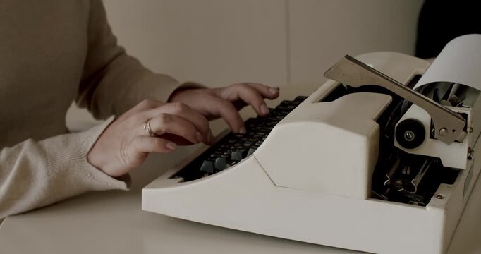 Woman's hands typing on a retro typewriter keyboard, her fingers pressing the keys to create a document. Slow-motion footage captures the classic mechanical process of old-fashioned writing