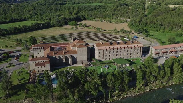 Wide aerial view of a large stone hotel complex with red tile roofs and pool, Catalonia, Spain