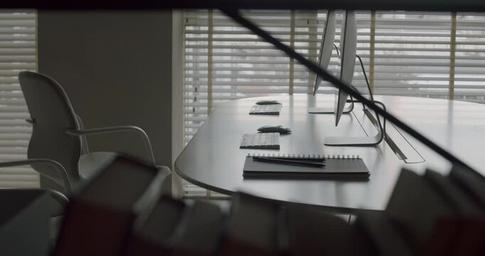 Modern empty corporate office or conference room with workstations, computers, and notebooks on a large table, showing a professional and minimalist interior for business meetings or presentations