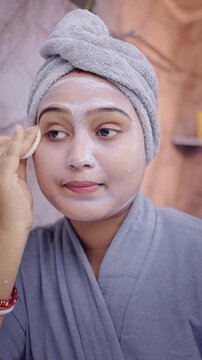 Indian woman gently removing facial mask with a cotton pad in bathroom, highlighting skincare, hygiene, and beauty routine.