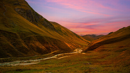 Obraz premium Scenic mountain valley with winding river under a colorful sunset sky