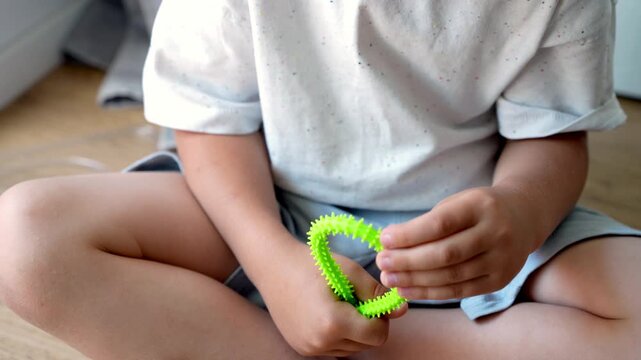 Close up footage of a childs hands playing with a green sensory fidget toy with flexible soft spikes, showing tactile stimulation, fine motor activity and sensory play.