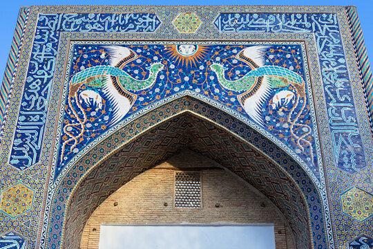 Ornate tiled portal of Nadir Divan-Begi Madrasah in Bukhara featuring mythical phoenix birds and sun face mosaic. Ideal for travel publications, cultural heritage articles, and architectural design.