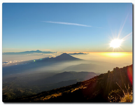 A breathtaking panoramic view captures a vibrant sunrise over a mountainous landscape, showcasing a sea of clouds and a distant volcano.
