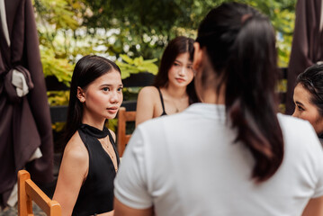 Obraz premium A young Southeast Asian woman listens attentively as a waitress confirms food and drink orders for her group at an outdoor restaurant.