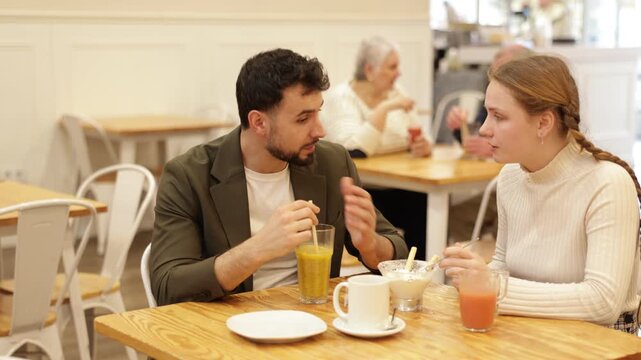 Teenage girl at a meeting with her dad in a cafe, they have an interesting conversation, eat delicious desserts and drink freshly squeezed juices. High quality 4k footage