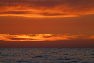 Fototapeta premium Dramatic orange sky with glowing clouds after sunset over the dark horizon of the sea
