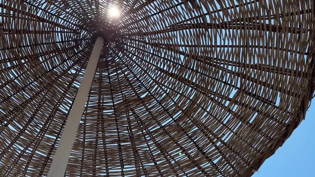 Low angle view looking up at a woven wicker beach umbrella against a clear blue sky during a sunny summer day