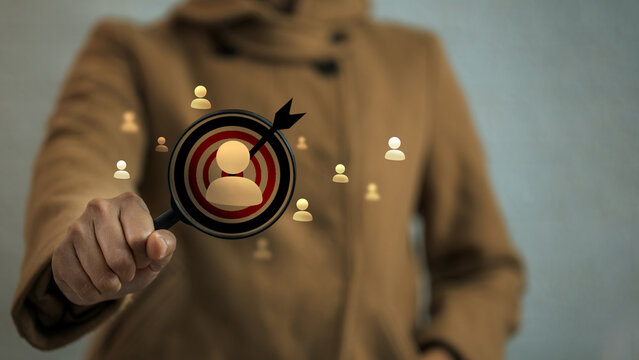 Person in brown coat holding magnifying glass focusing on user icon inside dartboard target