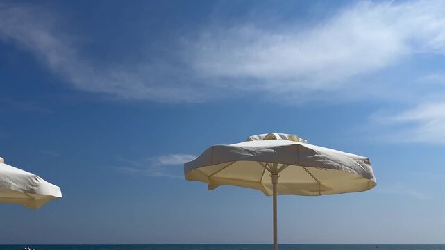 White fabric sunshade beach umbrella against a beautiful blue sky with wispy clouds over the calm sea horizon