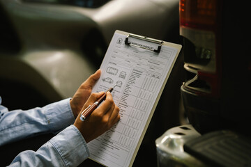 Naklejka premium Close-up of a vehicle inspector completing a car inspection checklist beside a damaged pickup truck, documenting condition for insurance claims, repairs, maintenance, and safety evaluation.