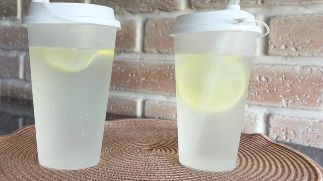 Refreshing lemonade with fizzy bubbles and lemon slice in a reusable plastic cup with straw, a perfect cold citrus summer drink for staying hydrated and healthy