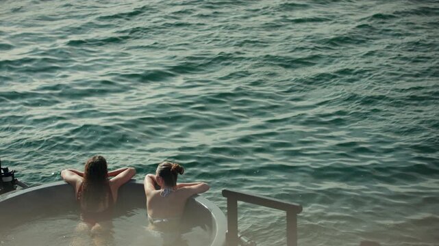 Relaxing women unwind in a hot tub beside the water