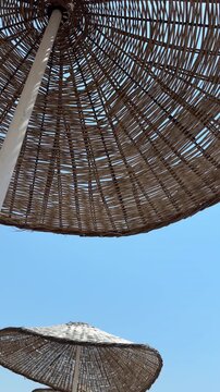 Low angle vertical perspective of woven wicker straw beach umbrellas against a vibrant blue sky during sunny summer weather