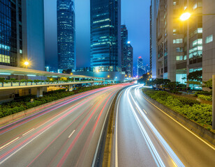 Fototapeta premium A long exposure photograph captures the vibrant streaks of light from moving vehicles along a wide city avenue, framed by towering skyscrapers under a twilight sky.