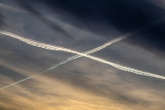 Two jet contrails forming a crossing X shape against an evening sunset sky