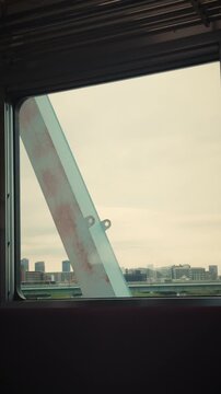 POV looking out the window of a moving train crossing a steel bridge with a distant city skyline and river