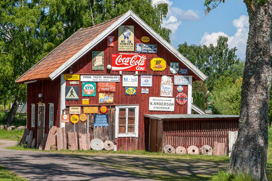 HJO, SWEDEN - JUNE 8, 2013: A traditional red wooden building exterior covered with a large collection of vintage metal advertising signs, including Coca-Cola, Mobil, and BP on a sunny day.