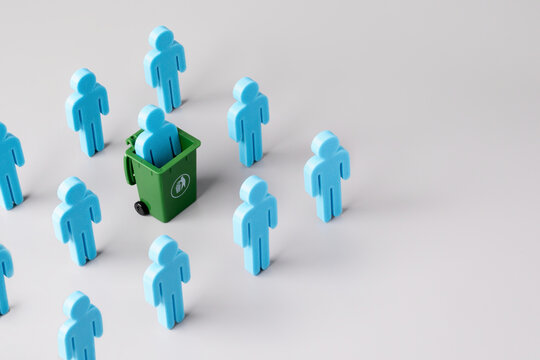 A blue figure in a green trash bin among a group on a grey background. Corporate layoffs, downsizing, employee termination, rejection concept. Copy space for text.