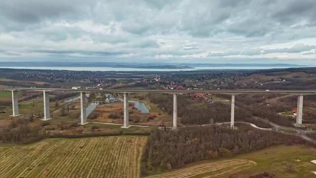 Hyperlapse drone view of the Kőr&ouml;shegyi V&ouml;lgyh&iacute;d in Somogy County, spanning the rural landscape near Lake Balaton as a modern concrete highway bridge under an overcast winter sky.