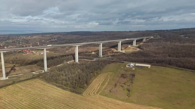 In Somogy County, the Kőr&ouml;shegyi V&ouml;lgyh&iacute;d spans the rural landscape as a long concrete viaduct on the M7 highway, crossing fields near Lake Balaton under a cloudy winter sky in a bird's-eye view.
