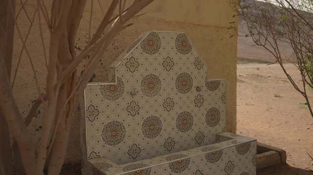 Patterned tile fountain bench beside leafless tree in desert setting in Morocco