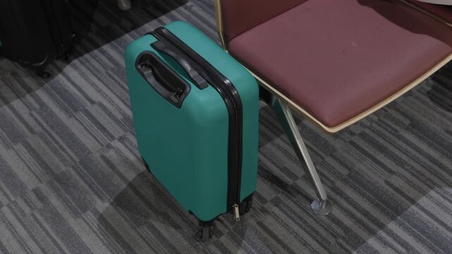 Green teal hardshell carry on suitcase standing beside a chair on patterned carpet floor