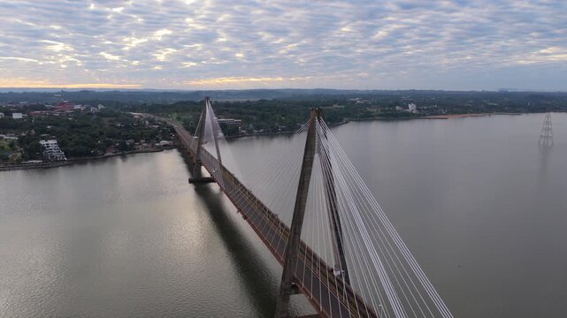 Cinematic drone orbit revealing the San Roque Gonzalez International Bridge connecting Argentina and Paraguay over the Parana River at dawn.