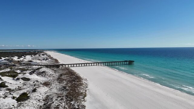 Drone orbit at pristine white sand coastline with the long St. Andrew State Park Pier stretches out to a beautiful end point, Panama City, Florida, US
