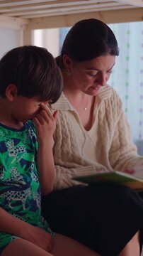 Mother guiding young son through storybook before bedtime in children&rsquo;s bedroom, highlighting early literacy, childhood learning, parental involvement and family connection
