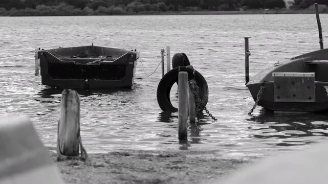 4K fixed monochrome shot of small fishing boats moored at the shore of the &Eacute;tangs palavasiens in Villeneuve-l&egrave;s-Maguelone, H&eacute;rault, capturing a timeless and serene waterfront atmosphere.