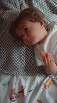 Young child enjoying nutritious fruit while lounging comfortably on bed, highlighting healthy eating, relaxation, childhood comfort and home life